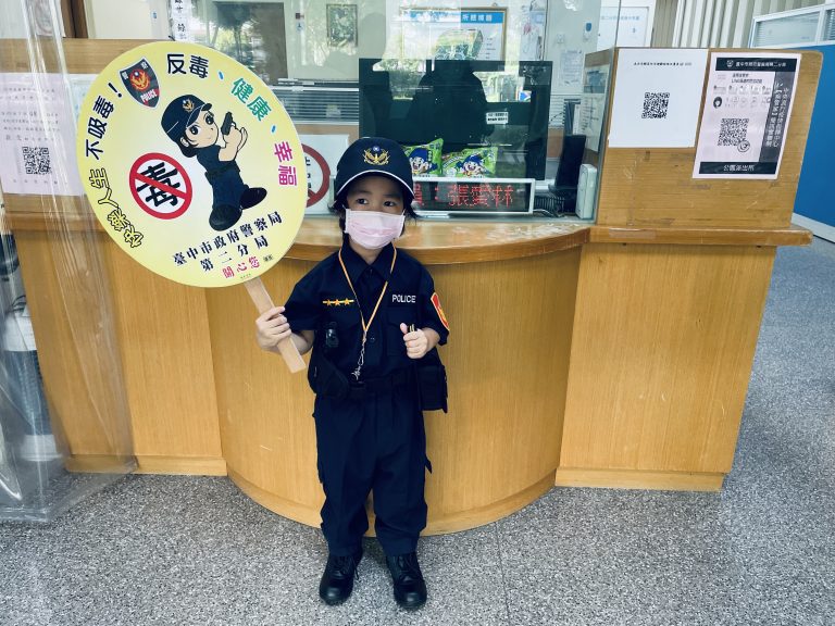 圖片說明：中市警二分局為了一圓張童警察夢，除介紹應勤裝備也讓坐上值班台拍照留念，張童手持反毒宣導牌站在值班台前供員警攝影，架式十足。(記者林㤈輝翻攝)