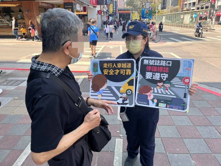警員手舉標語在路口對行人做交通安全宣導。（記者林金聖翻攝）