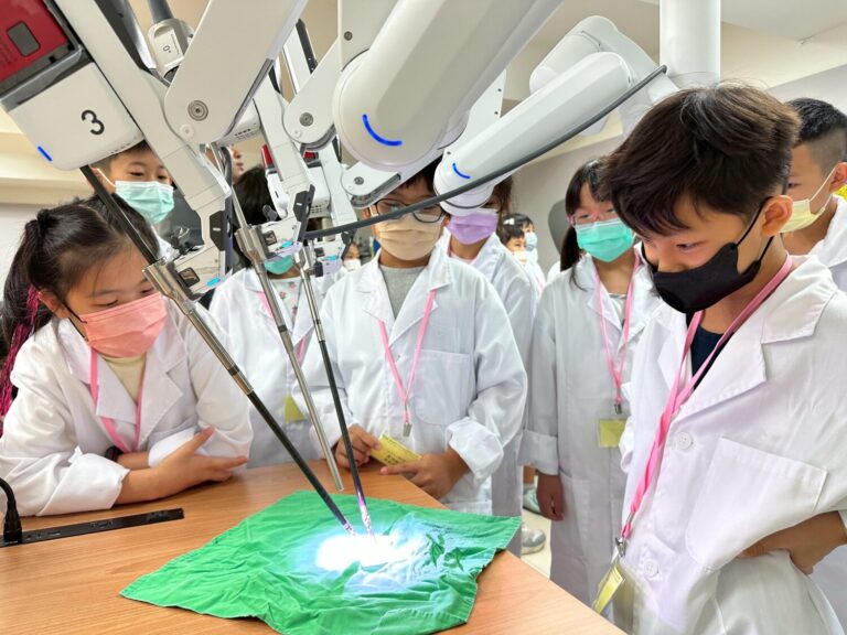 40位小小醫師體驗營專注地操作達文西機械手臂，在綠色布料上進行模擬手術，學習微創手術技術。場景展現智慧醫療啟蒙的主題，學生們在醫療與科技教育環境中，親身體驗醫療職涯的奧妙。（圖/記者張家燁翻攝）